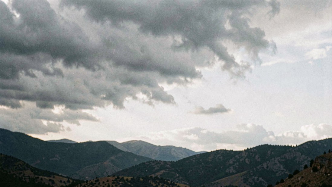 Une moitié de ciel couverte de nuages gris au-dessus d’une ligne de collines sombres, découpage net entre zone couverte et zone claire, lumière froide.