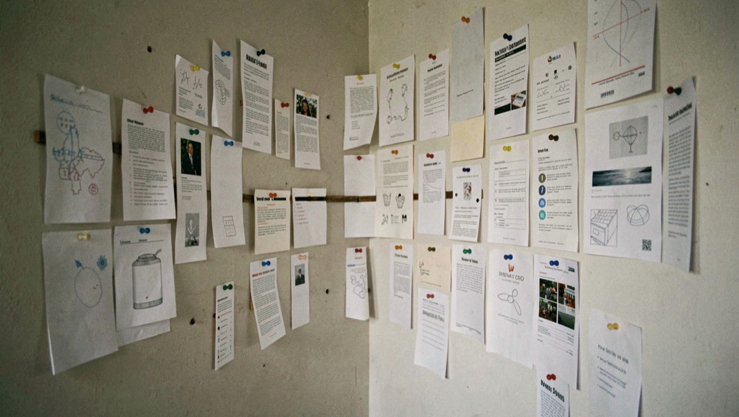 Des gabarits de papier de tailles variées punaisés sur un mur en quinconce, disposés autour d’un axe horizontal imaginé, lumière de travail, plan large.